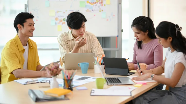 A young team of professionals collaborating in a casual meeting room setting, brainstorming around laptops and documents — representing modern outsourced accounting services in the Philippines.